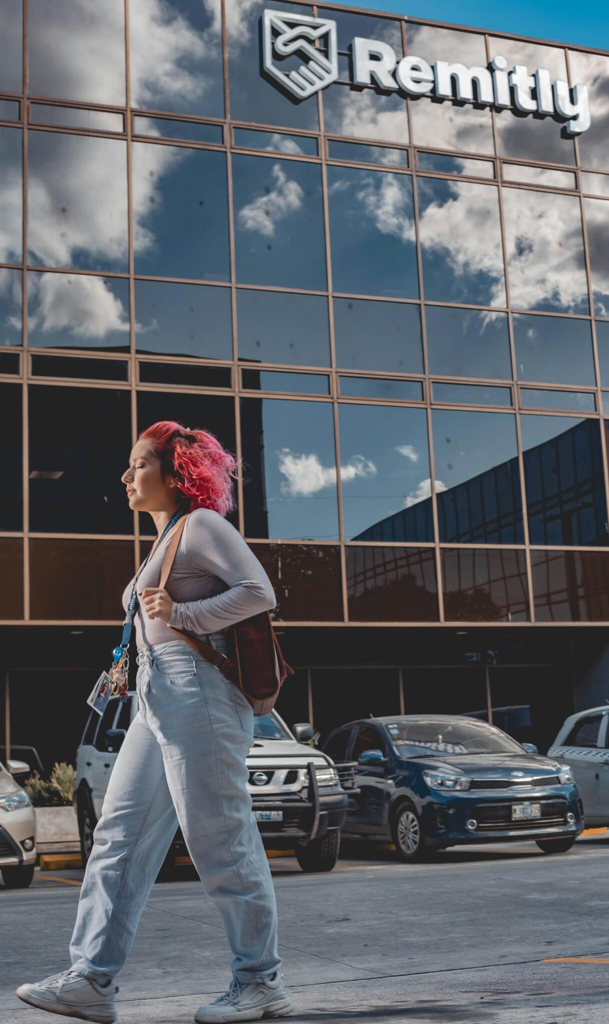 A young woman with pink hair walks past an office building reflecting the sky in Managua, Nicaragua.
