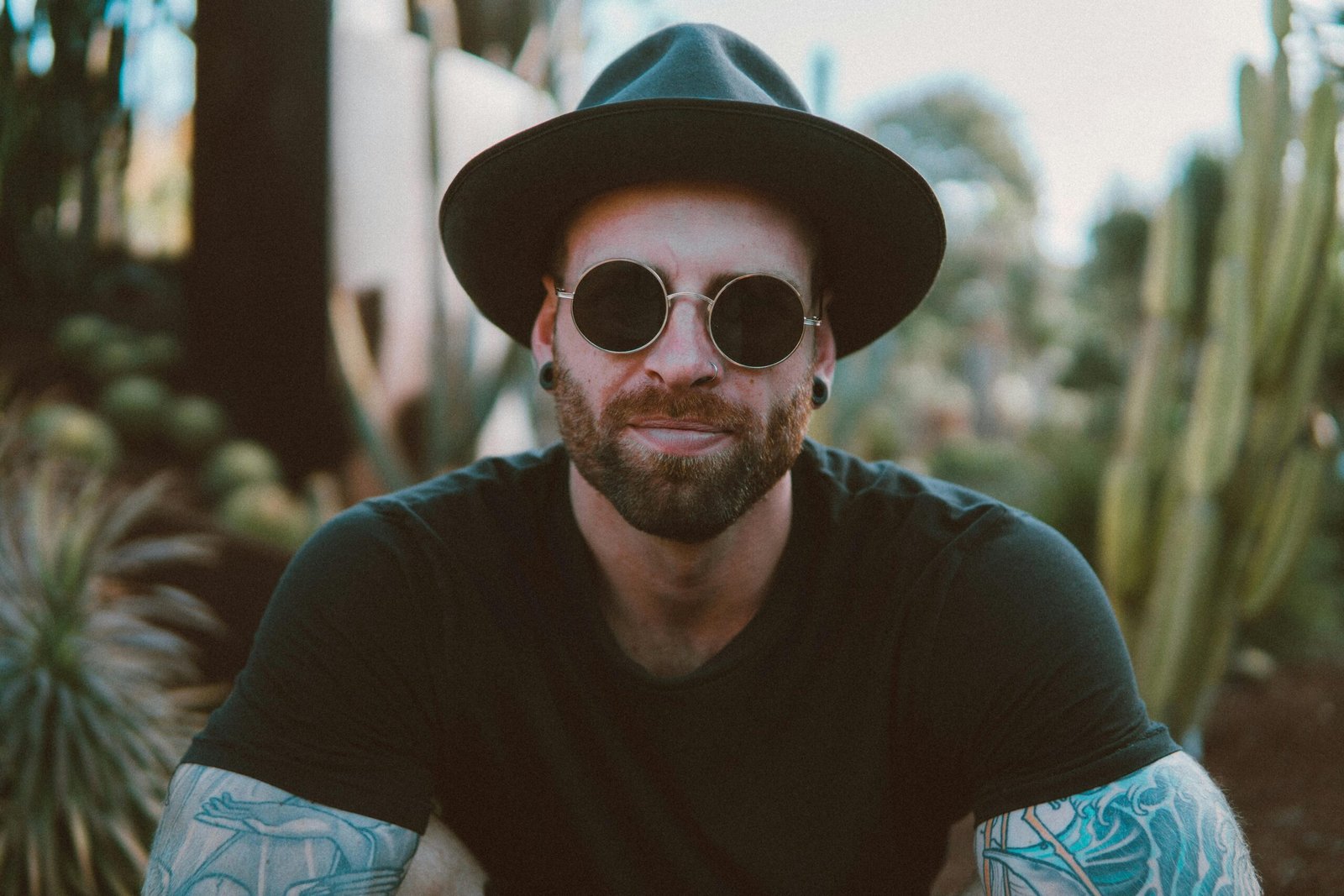 Stylish man with beard and tattoos wearing sunglasses and a hat, enjoying outdoors.