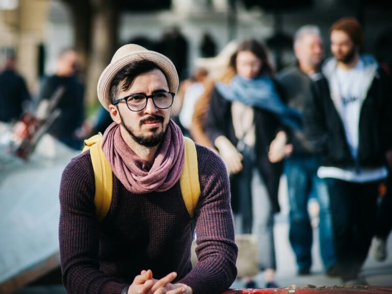 A stylish man in a trendy outfit stands out on a busy city street with various people in the background.