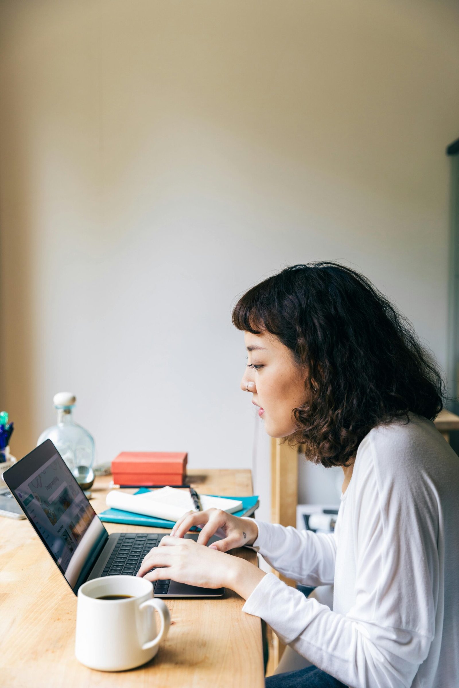 Side view of concentrated young female freelancer sitting at table and browsing laptop while working on business strategy during weekend and drink coffee