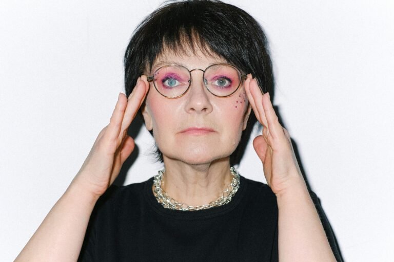 Close-up portrait of a senior woman with vibrant makeup and eyeglasses, exuding confidence.
