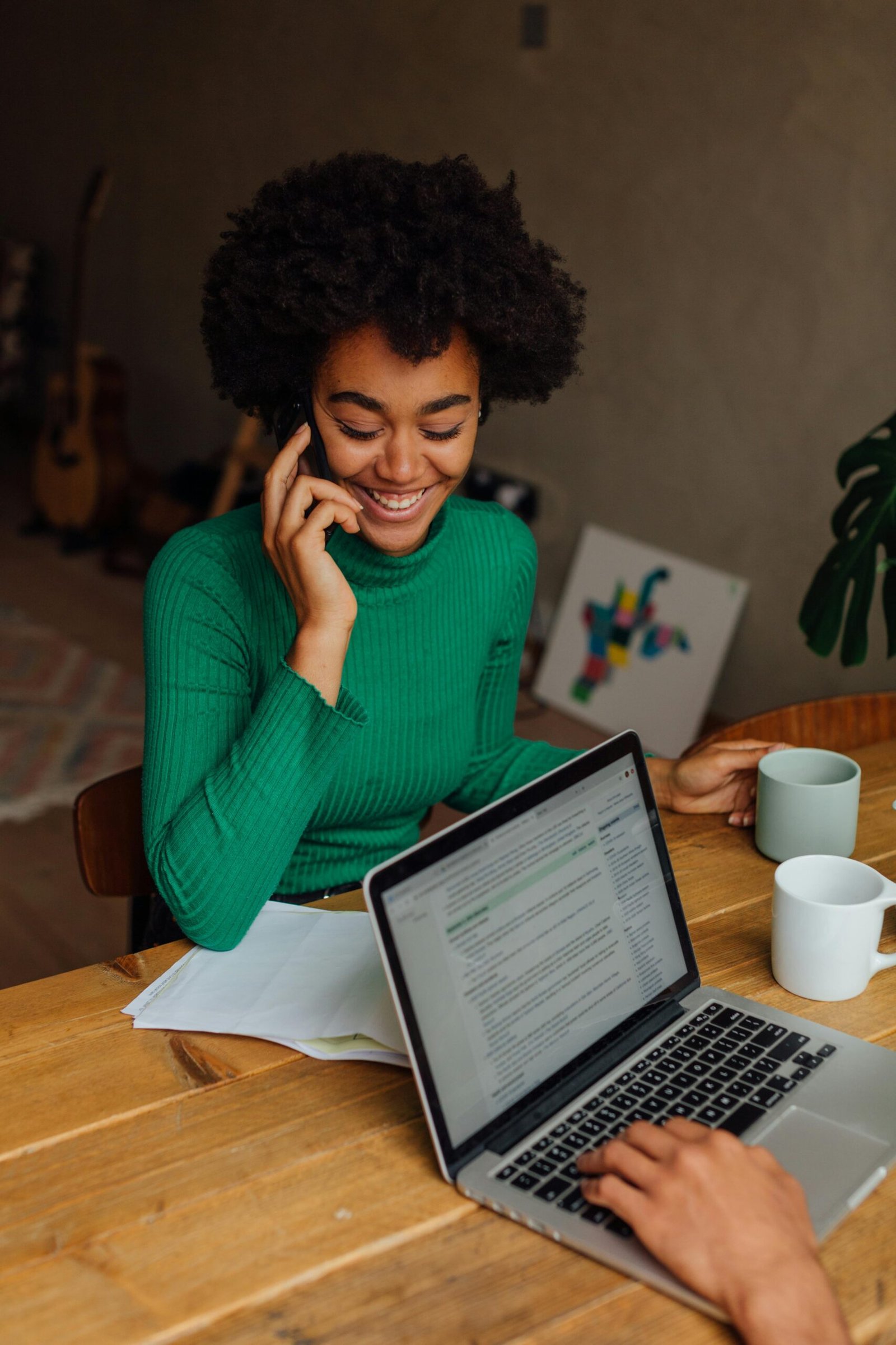 African American woman with afro hair talking on phone and holding a mug indoors.