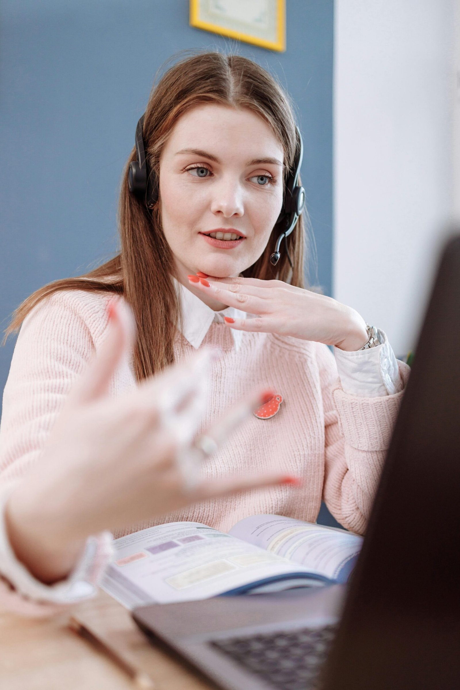 Woman wearing headset teaches online using a laptop from home, engaging in a virtual lesson.