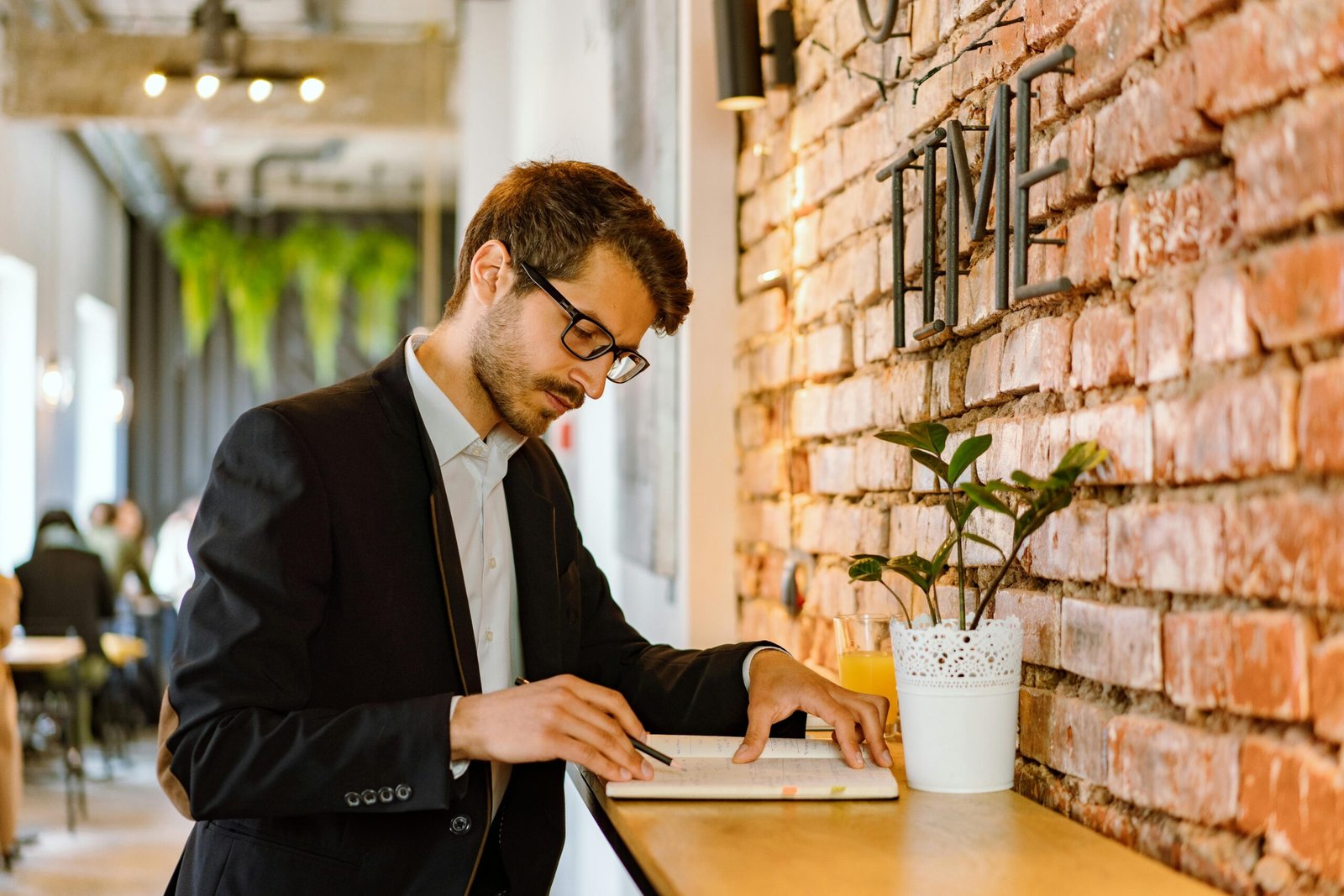A professional man in a café setting taking notes in his planner, concentrating deeply.