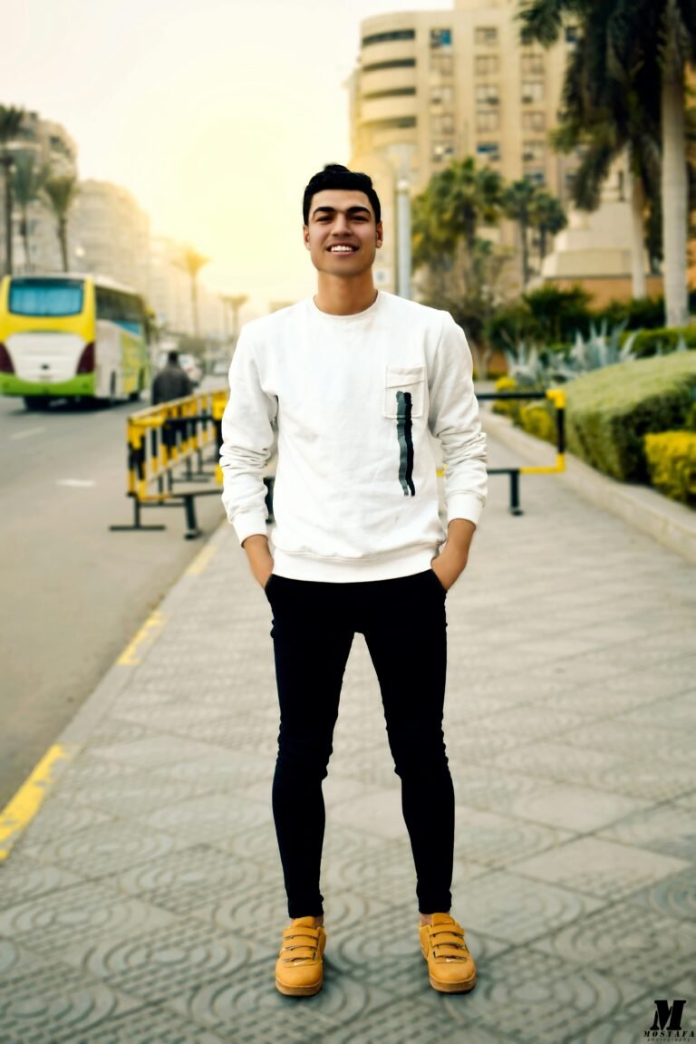 Smiling young man posing confidently on a city street during the day.